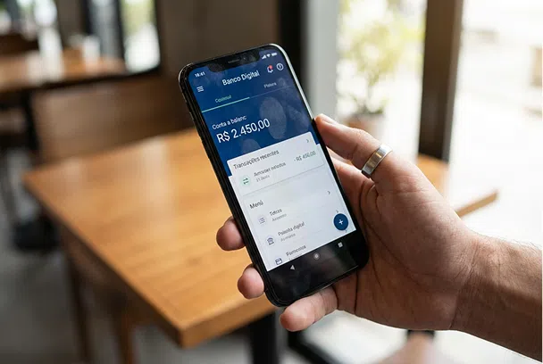 Mão segurando smartphone exibindo aplicativo de banco digital.