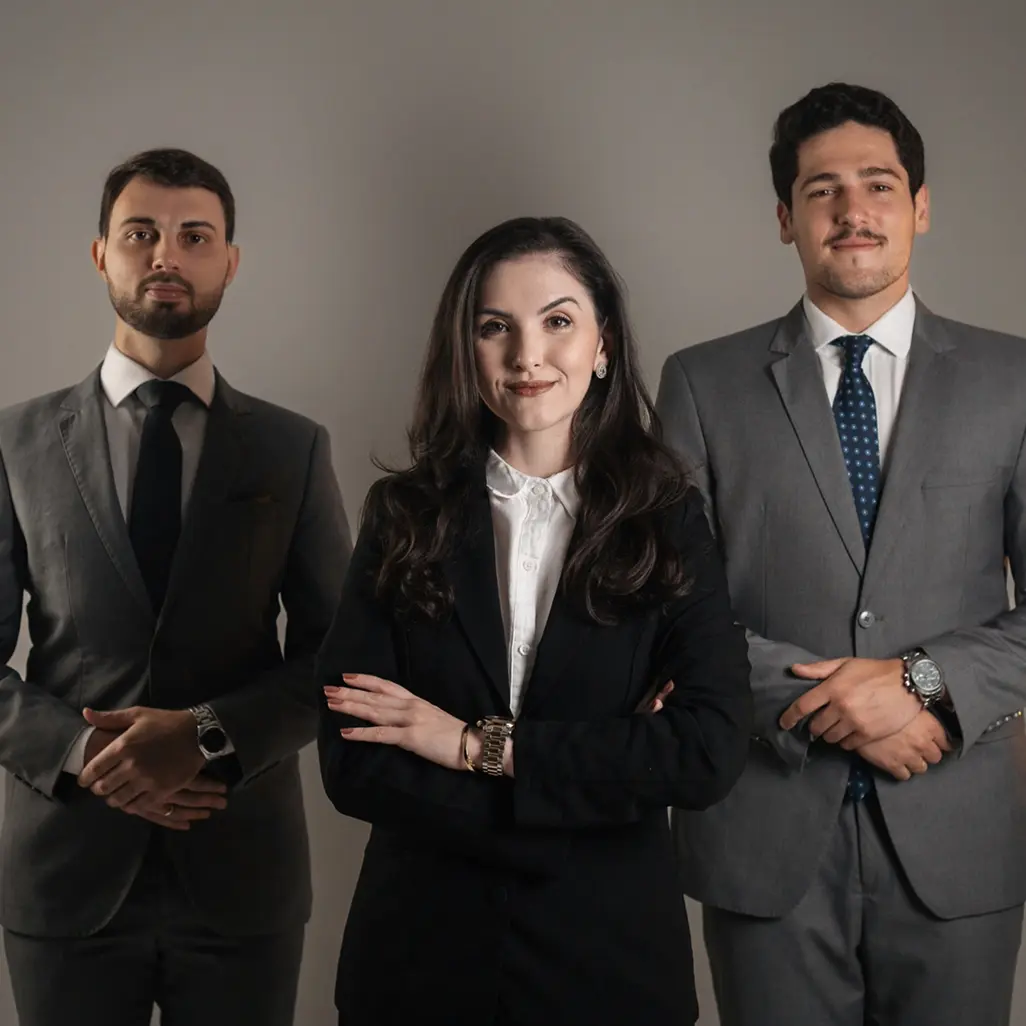 Time de advogados sócios: Maria, Arthur e Marcelo em trajes sociais contra fundo cinza.